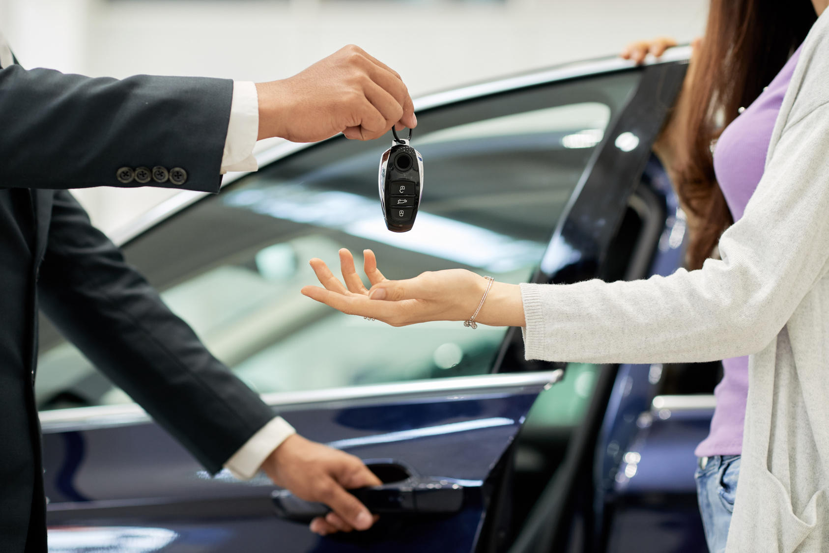 two hands exchange car keys against a car background